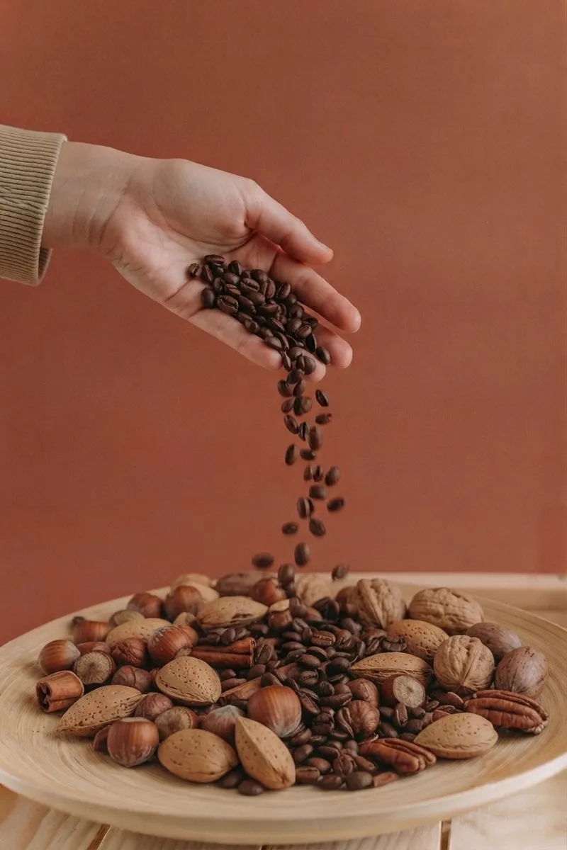 Hand pouring coffee beans over a plate of mixed nuts